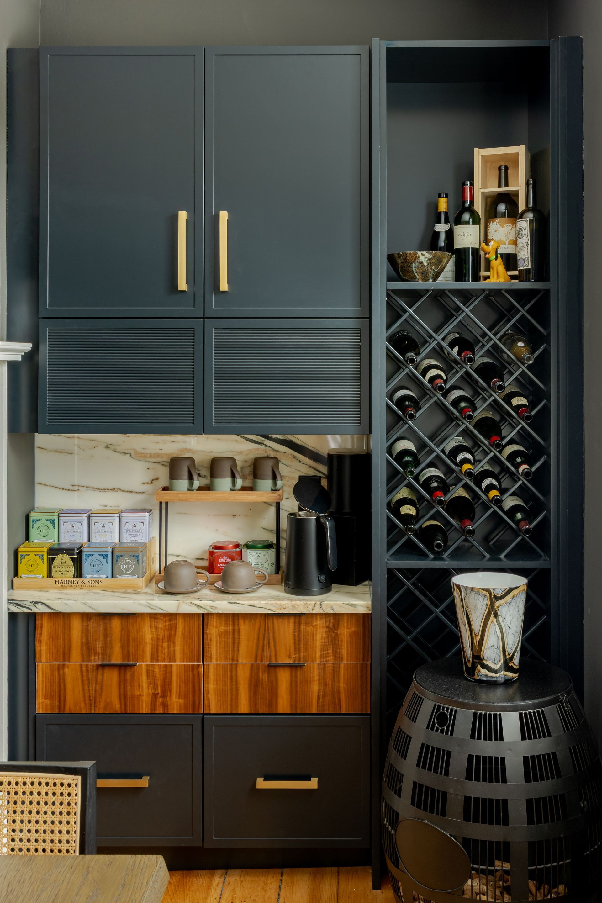 A dark blue built-in coffee and wine bar featuring wood-grain drawers, brass pulls, and a latticed wine storage rack.