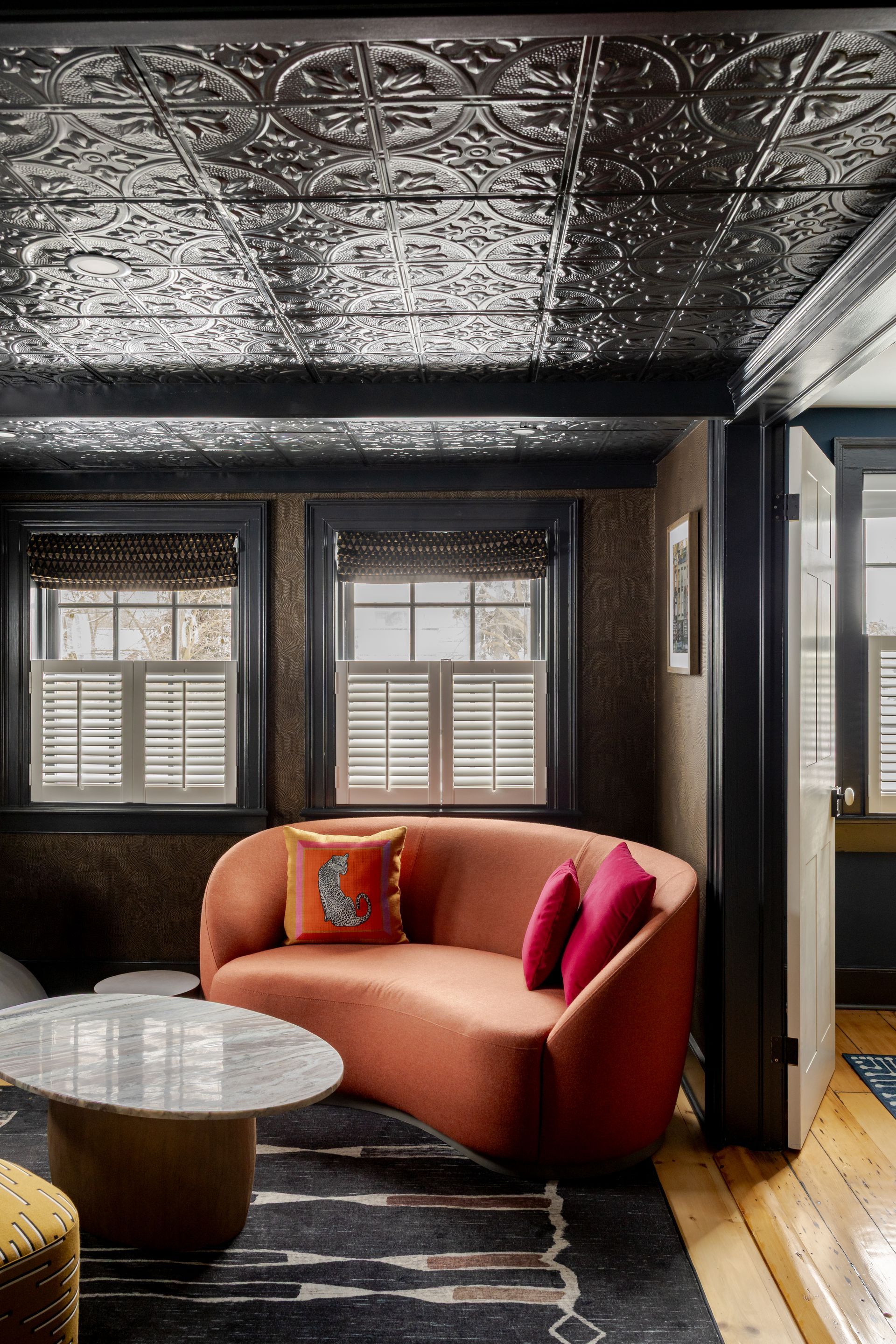 A curved, rust-orange sofa sits on a dark patterned rug under a metallic, decorative tin ceiling in a moody room.