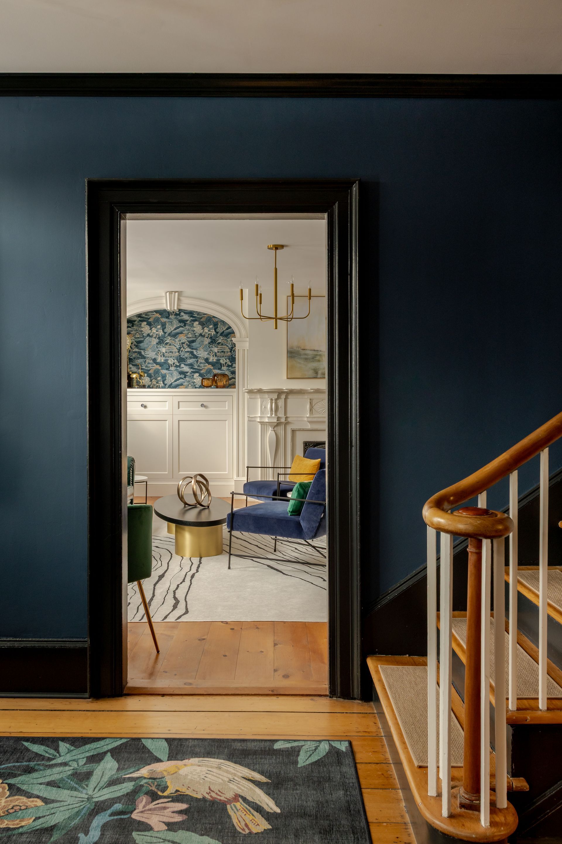 View through a dark blue entryway into a brightly lit living room with patterned decor and a wooden staircase.