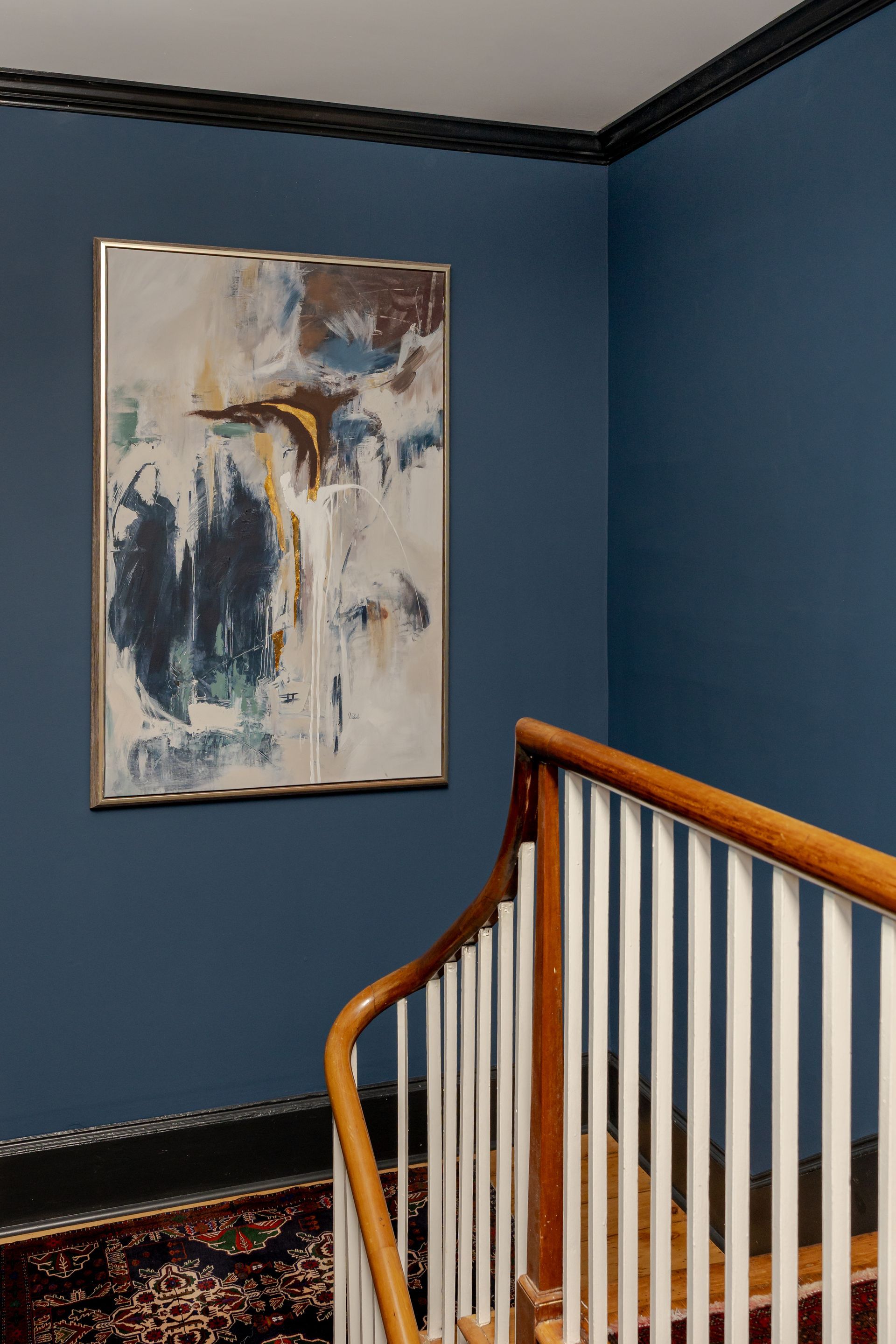A blue-walled stairwell featuring a modern abstract painting, white railings, and a patterned rug.