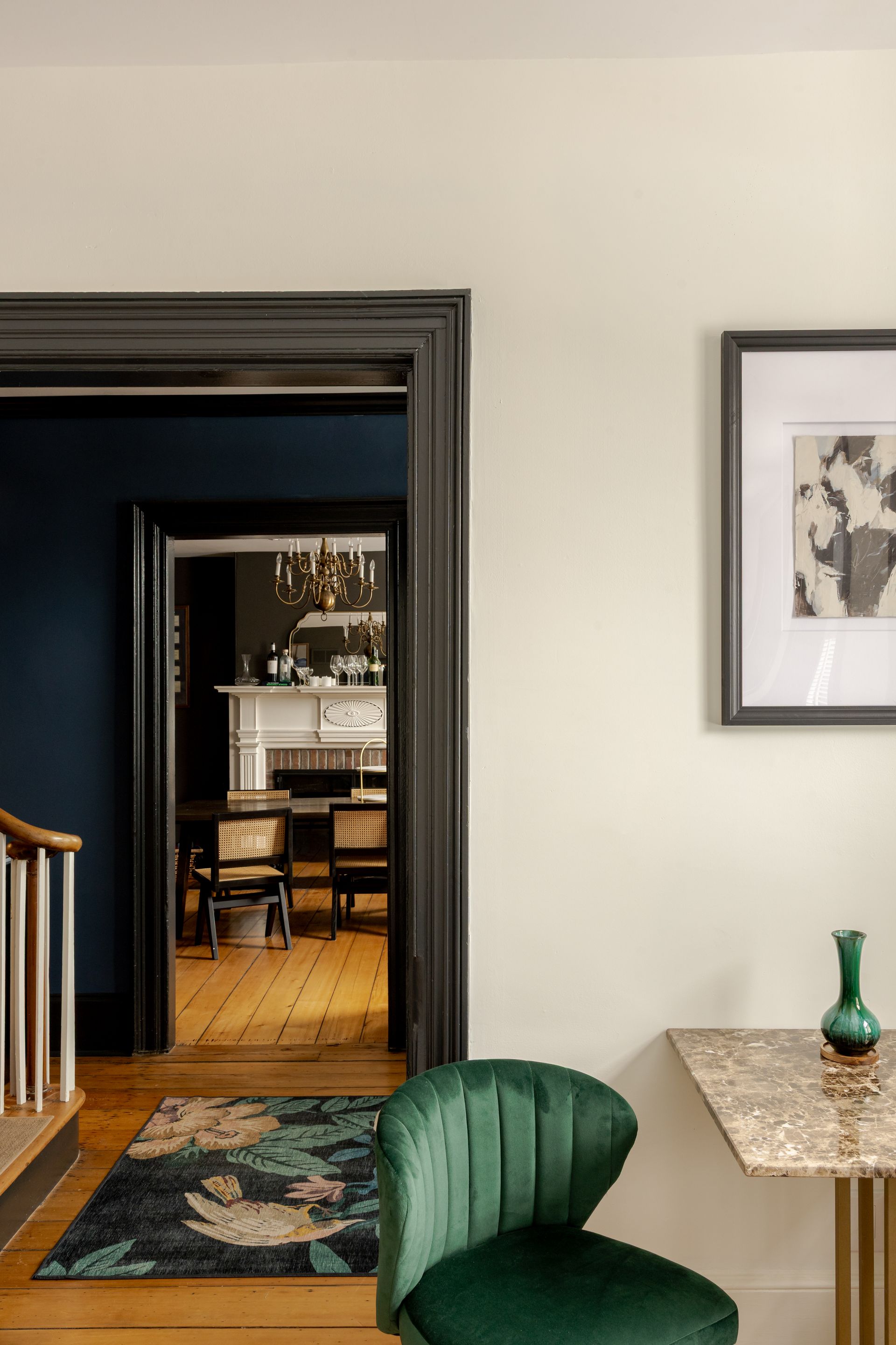 A green velvet chair sits next to a marble table in an elegant room, with a view into a dark-walled dining area beyond.