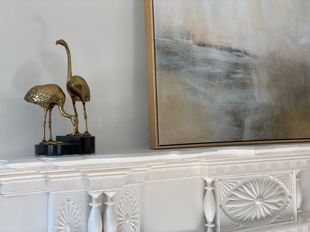 Golden flamingo sculptures on a white mantel with artwork in the background.