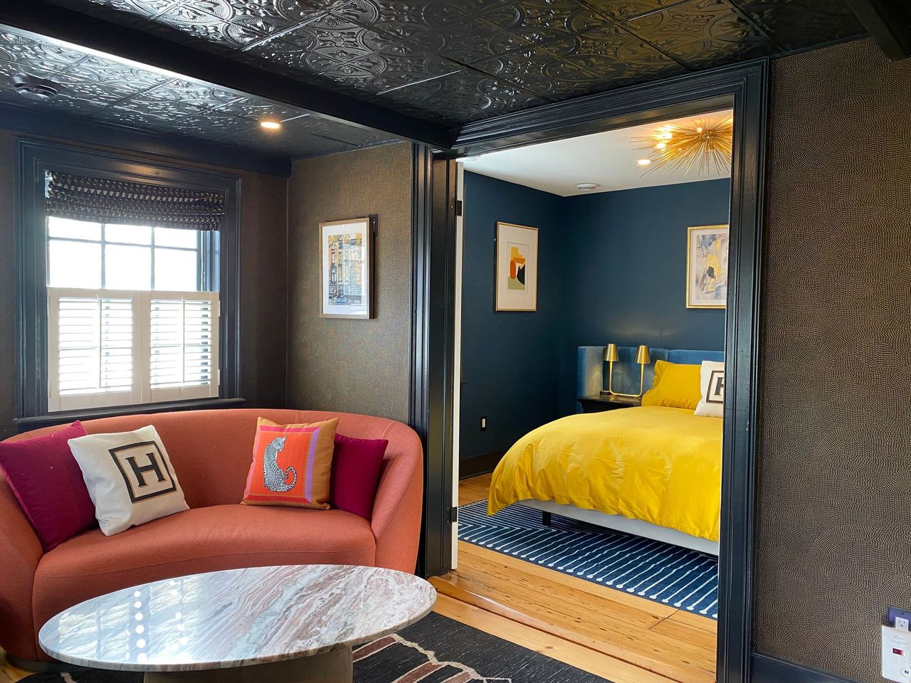 Living room with orange sofa, marble table, and doorway to a blue bedroom with yellow bedding.