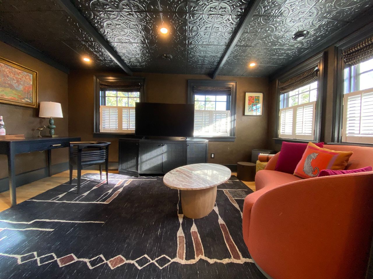 Cozy living room with dark walls, patterned rug, orange sofa, and black ceiling with recessed lighting.