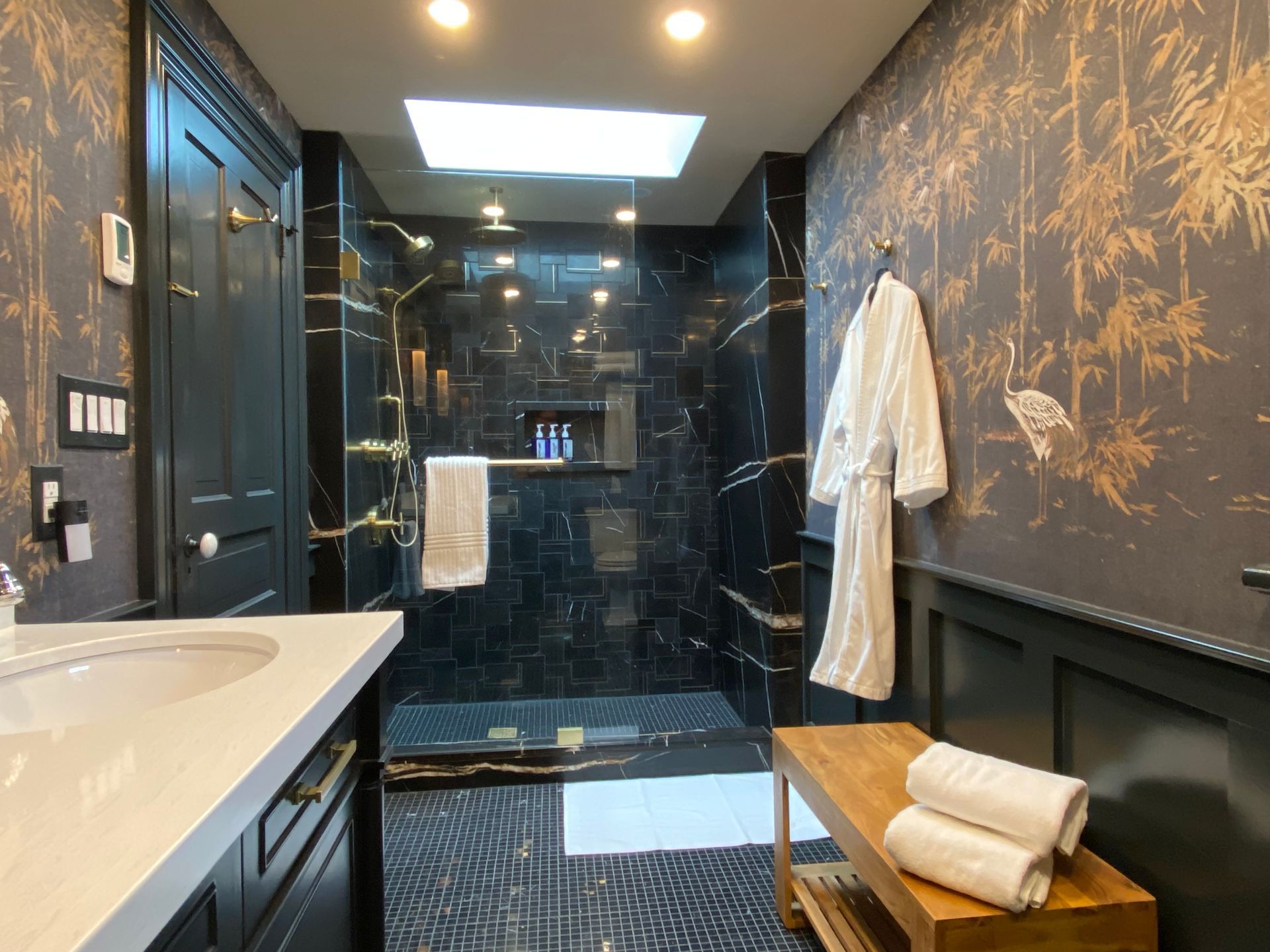 Luxurious bathroom with black marble shower and gold accent wallpaper, white robe on wall.