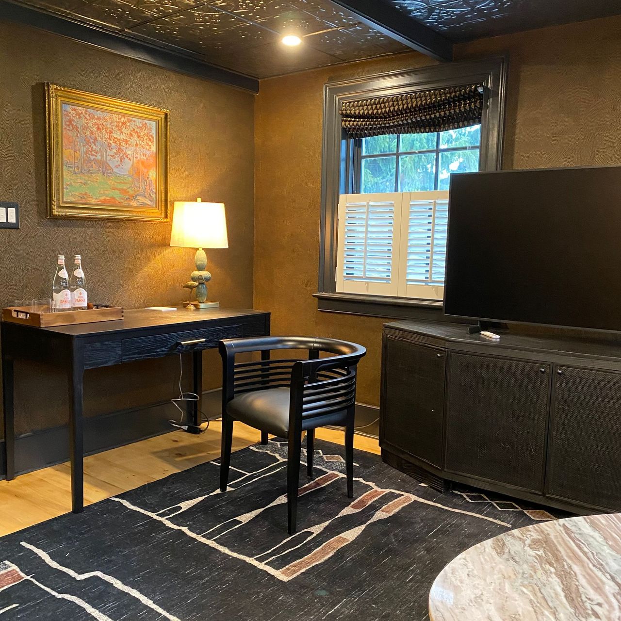A room with desk, chair, rug, and TV. Walls are textured. Dark furnishings.