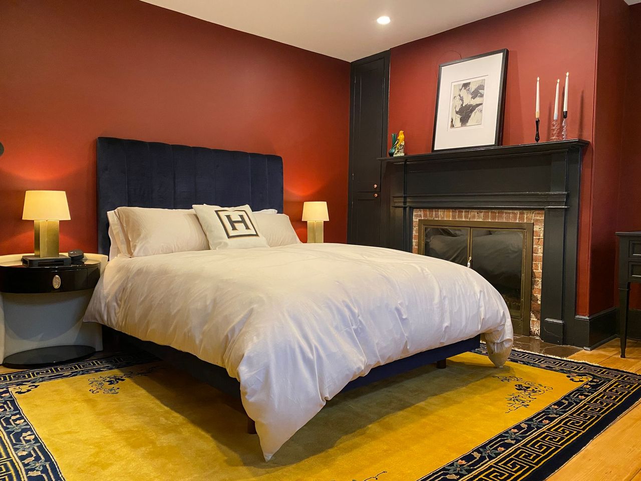 Bedroom with a navy bed, red walls, black fireplace, and yellow rug.