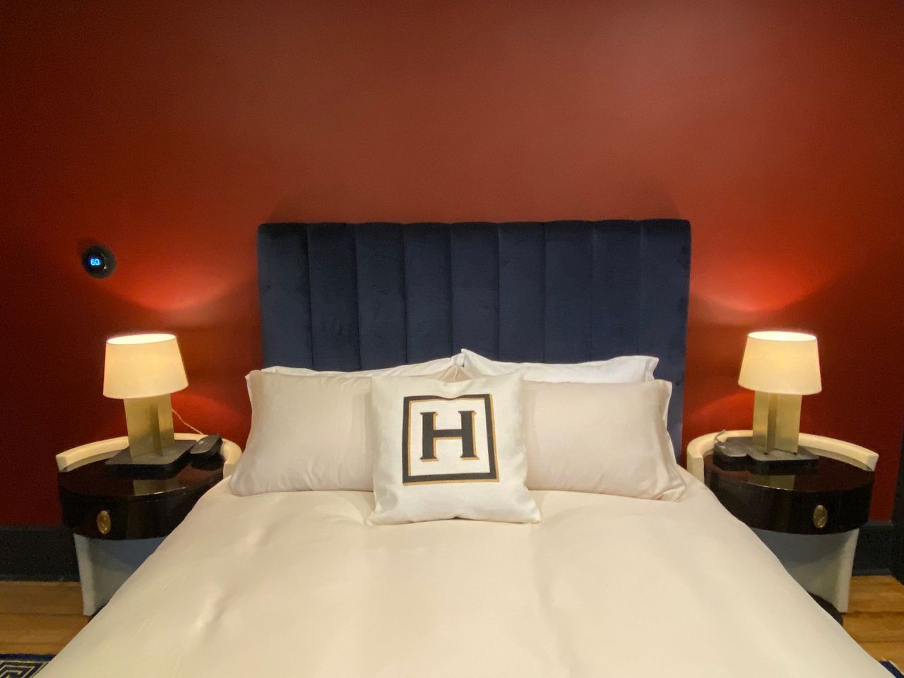 Bedroom with a blue headboard, cream bedding, and bedside tables with lamps, set against a red wall.