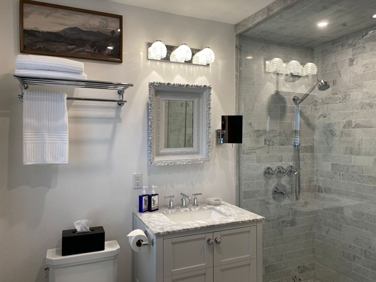 Bathroom with white vanity, shower, and towel rack; gray walls, marble tile, and a framed painting.