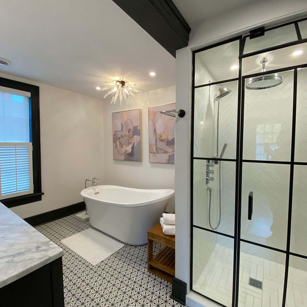 Stylish bathroom with a white tub, black-framed shower, and patterned floor.