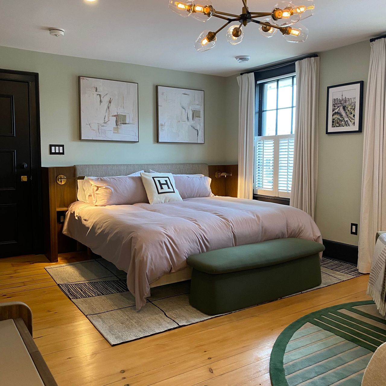 Bedroom with sage walls, wooden floors, a bed with pink bedding, and a green bench at the foot.