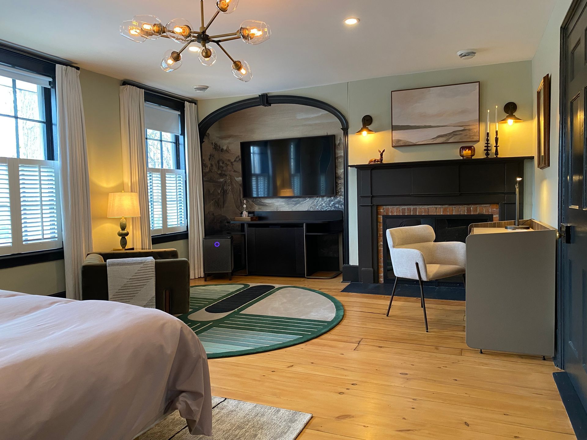 Bedroom with a light green wall, black fireplace, round rug, and a large bed.