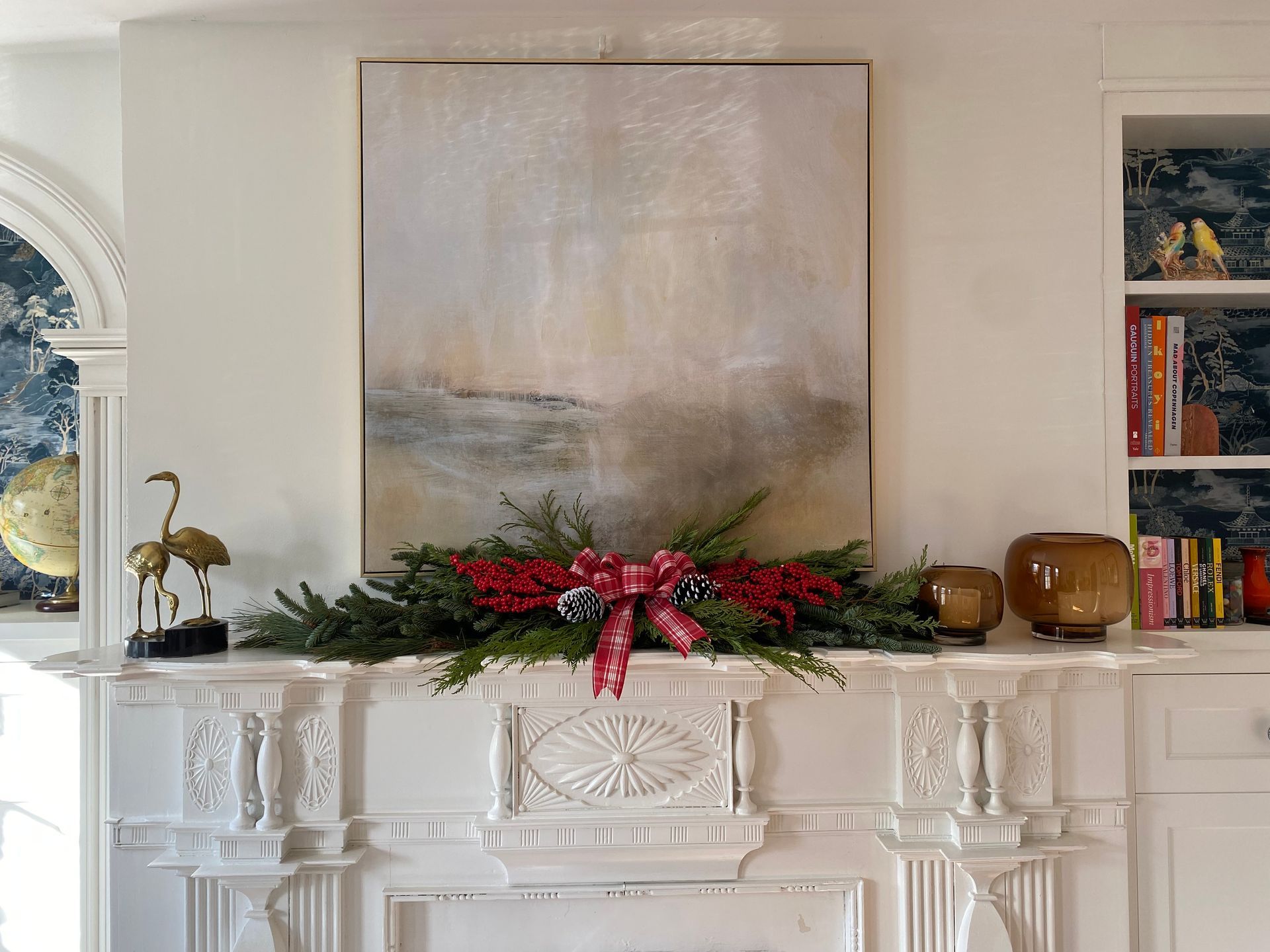 White fireplace mantel from 1792 decorated for holidays with painting and greenery.