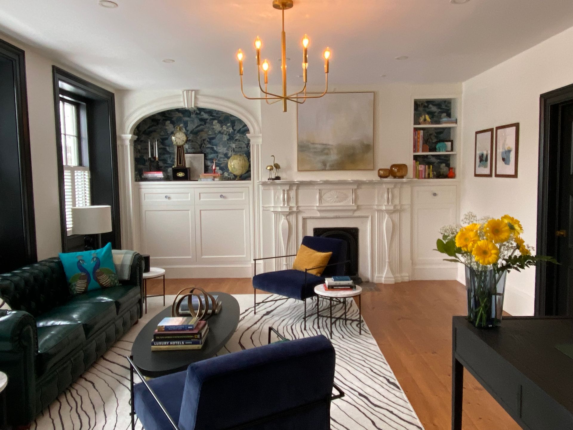 Living room with a fireplace mantel from 1792, green leather sofa, blue chairs, and a black and white rug.
