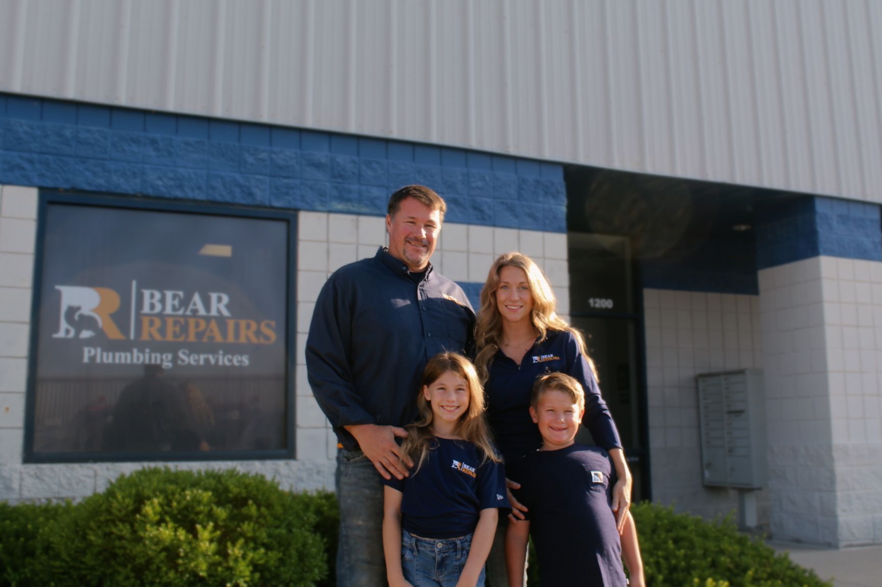 Two blue and white Bear Repairs plumbing service vans parked on pavement under a blue sky.