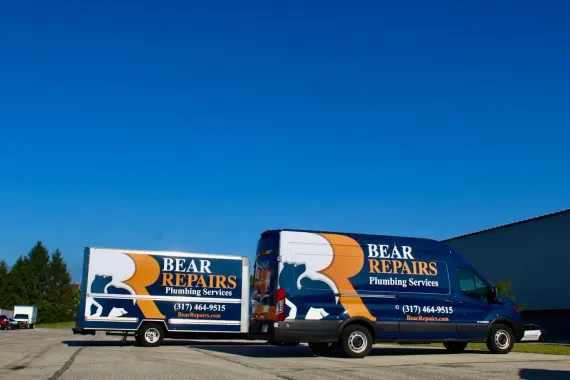 Two blue and white Bear Repairs plumbing service vans parked on pavement under a blue sky.