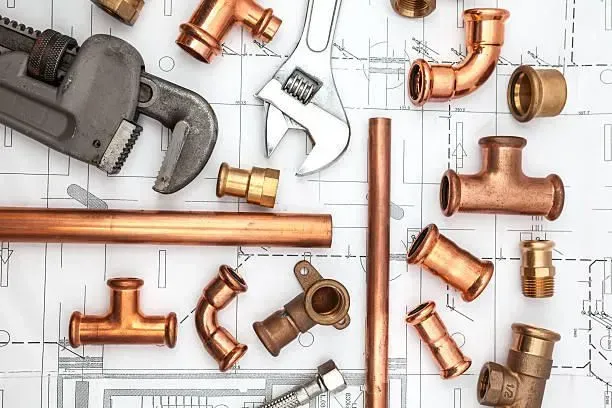 Plumbing tools and copper pipes on a blueprint, including wrenches and various fittings.