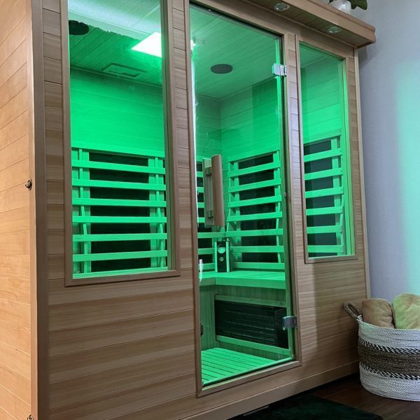 A wooden sauna with green lights and a basket on the floor.