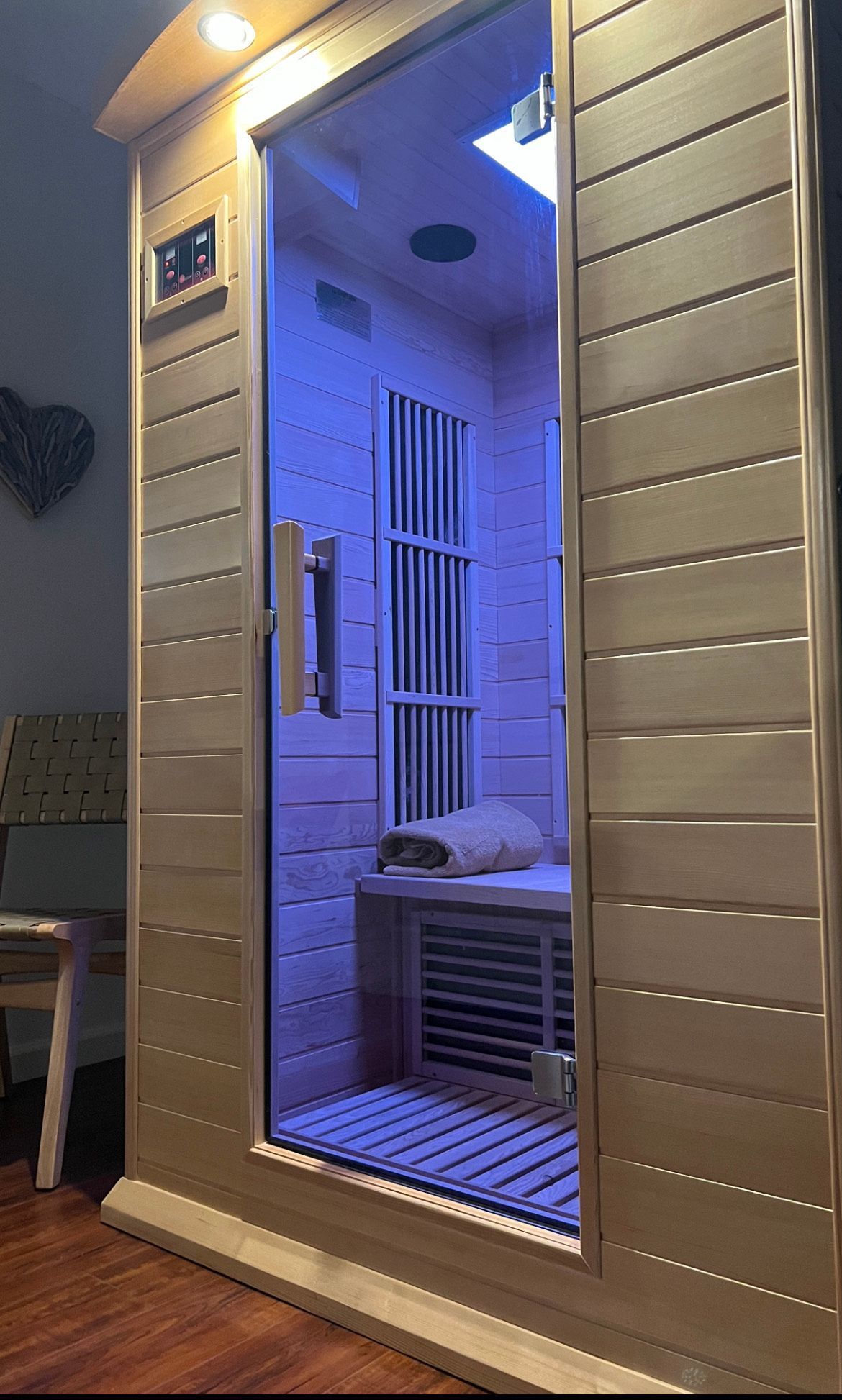 A wooden infrared sauna is sitting in a room next to a chair.