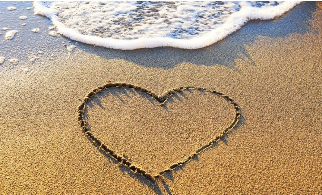 A heart is drawn in the sand on the beach.