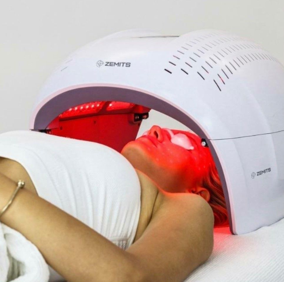 A woman is laying in front of a red led light device.