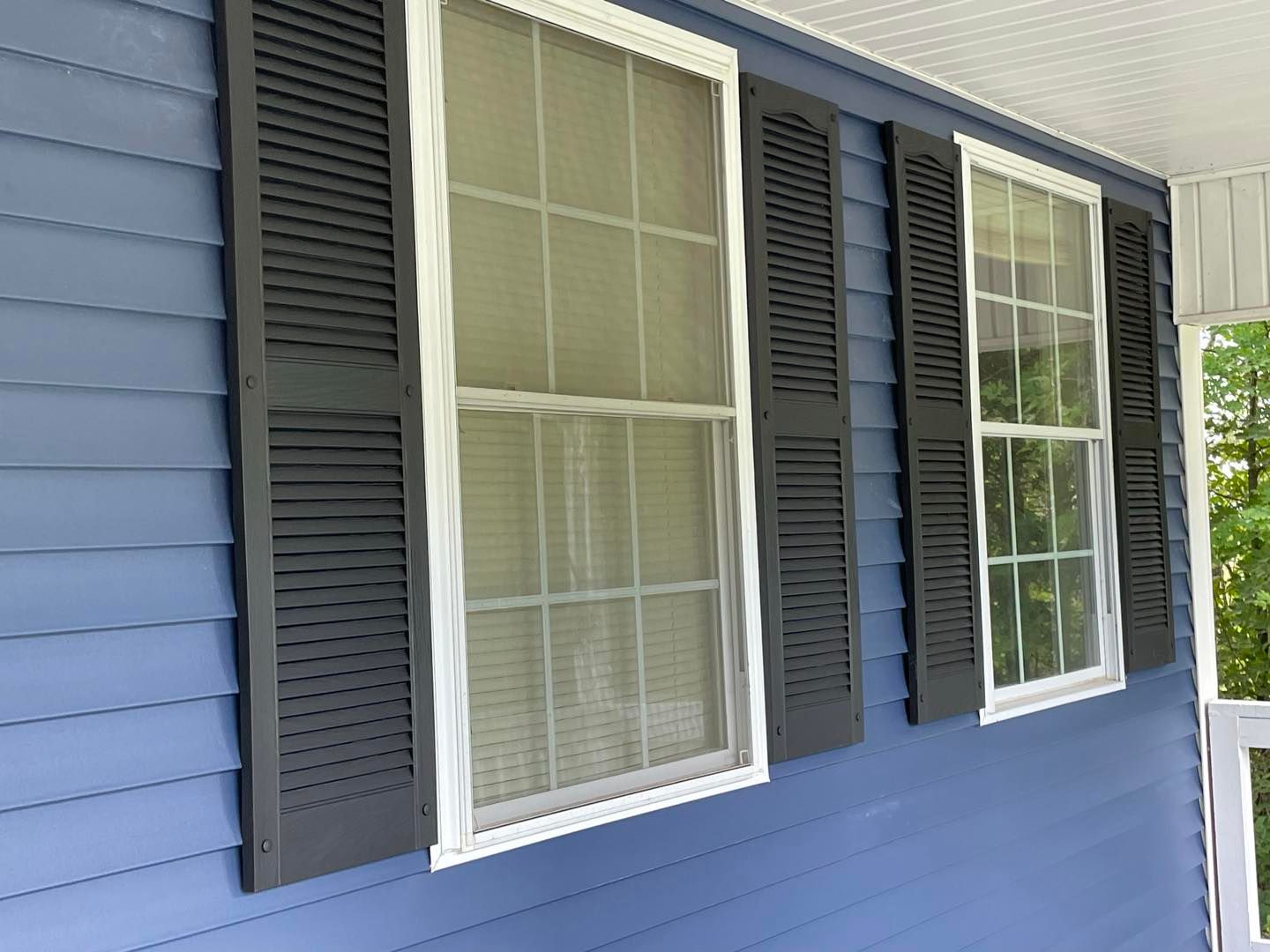 Blue house siding with white-framed windows, black shutters.