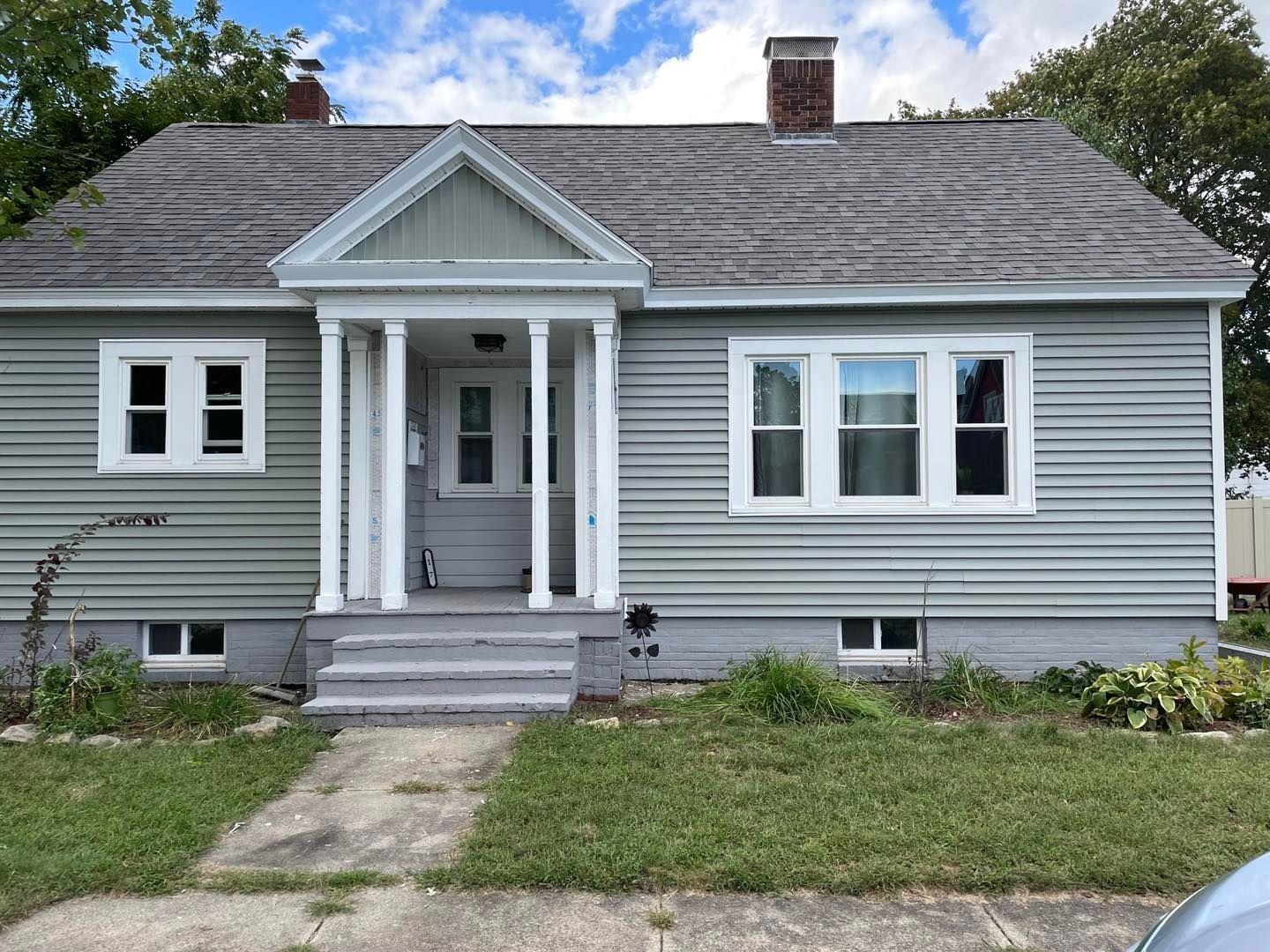 A light green house with white trim and a concrete walkway and steps, front yard with grass.