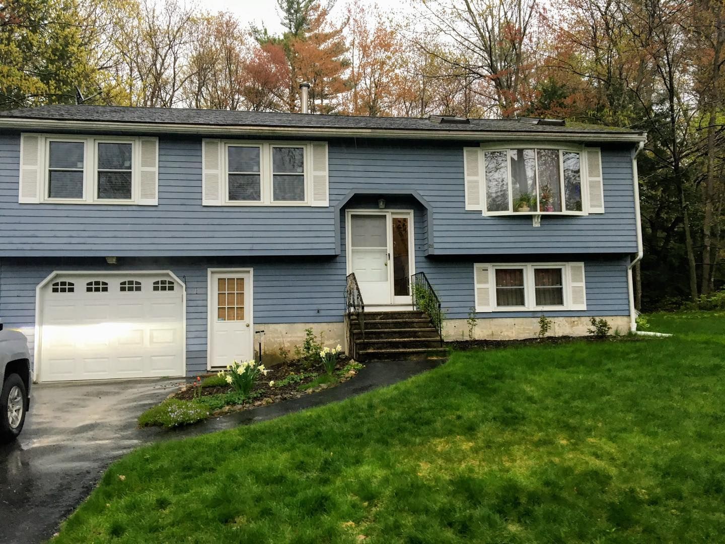 Blue split-level house with white trim, garage, and lawn; overcast sky.