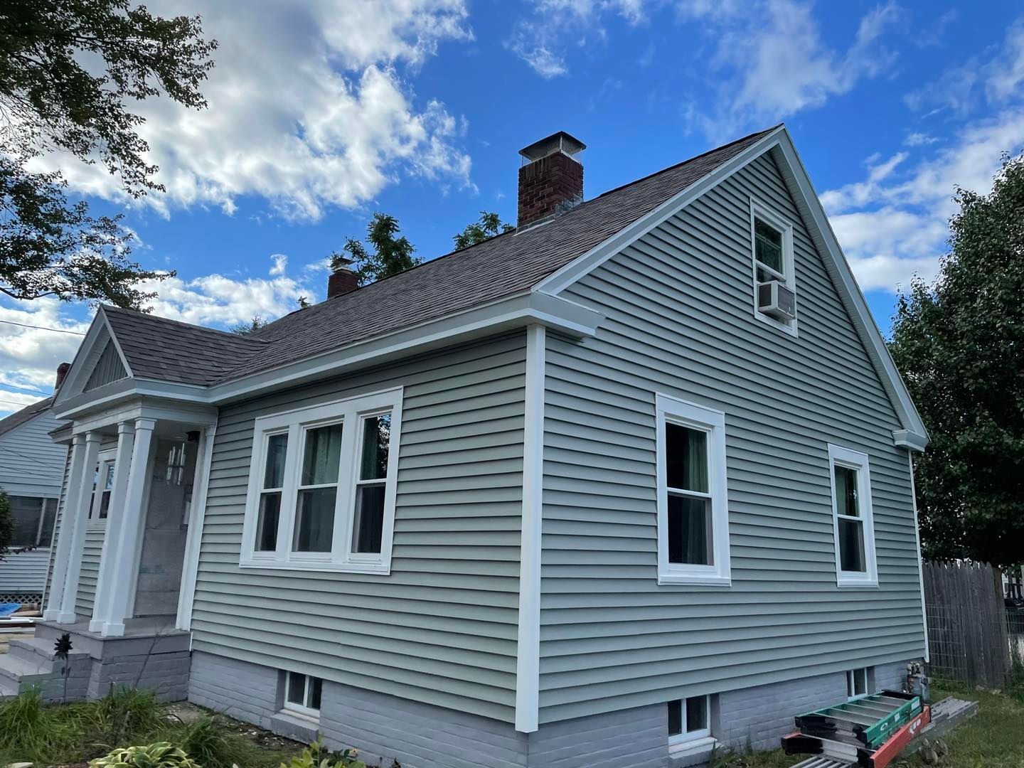 Green-sided house with white trim and dark roof under a partly cloudy blue sky.