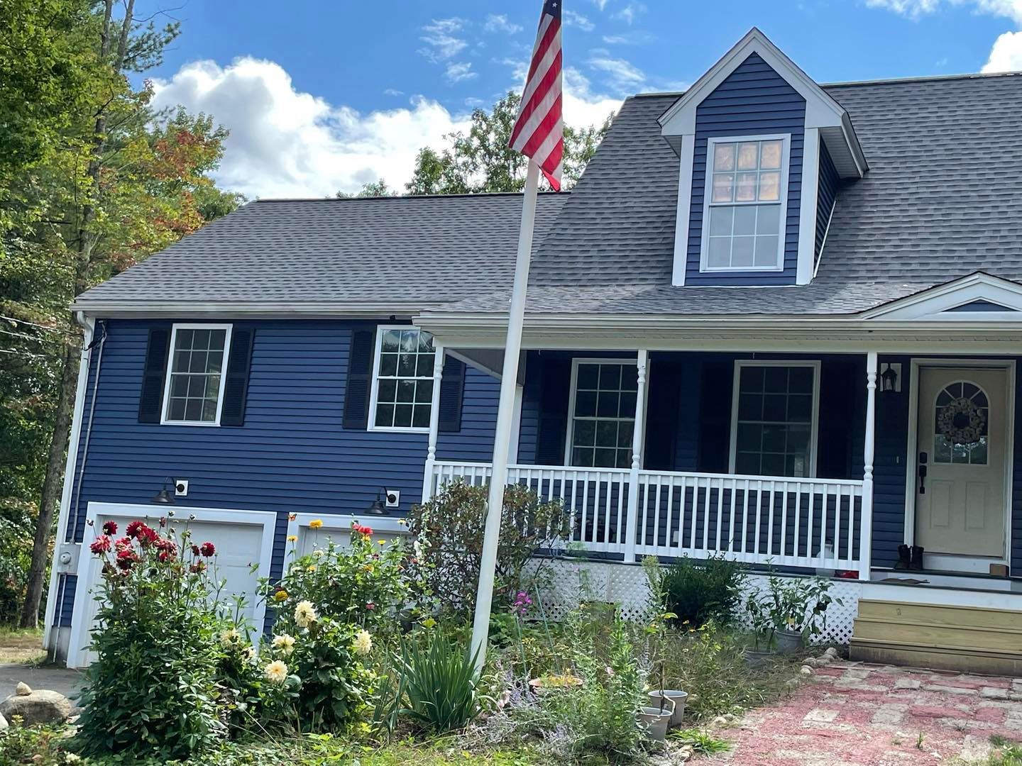 Two-story blue house with American flag; garden in front, cloudy sky.