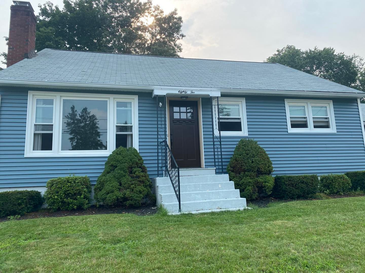 Blue ranch house with white trim, brick chimney, and front lawn.