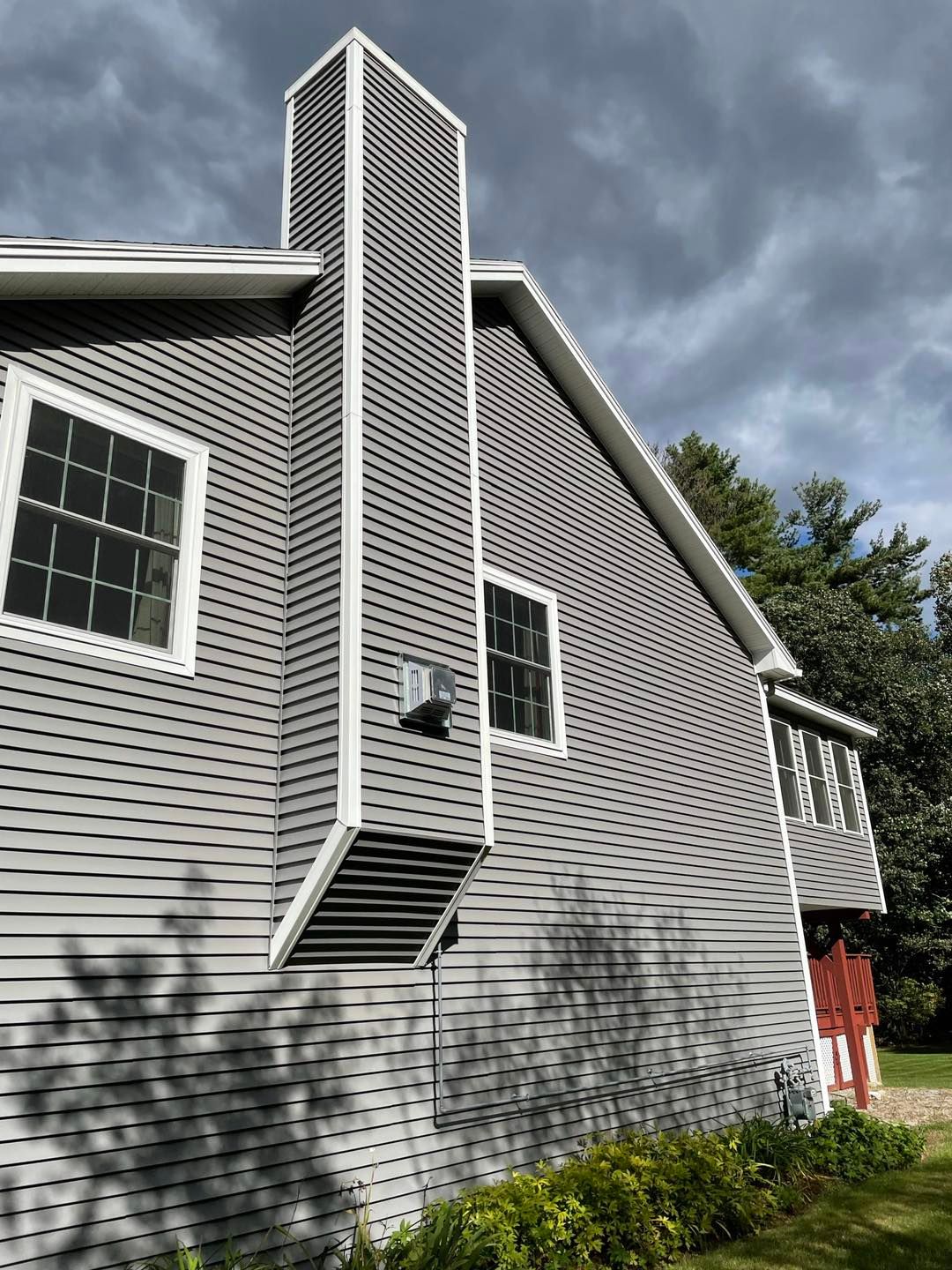Gray house with a tall, gray chimney. Two windows are visible, with a cloudy sky.