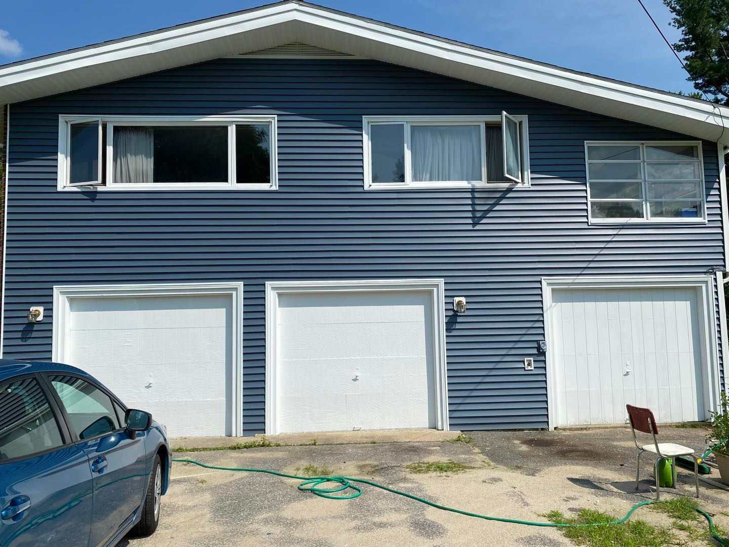 Blue house with three garage doors; windows above. A car and hose sit in the driveway.