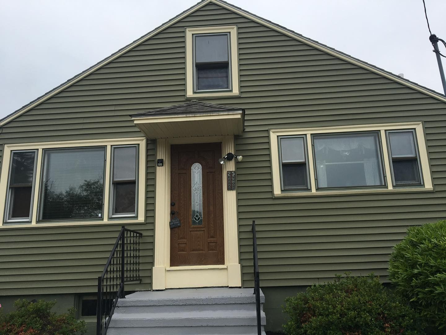 Green house with tan trim, brown door, and gray steps.