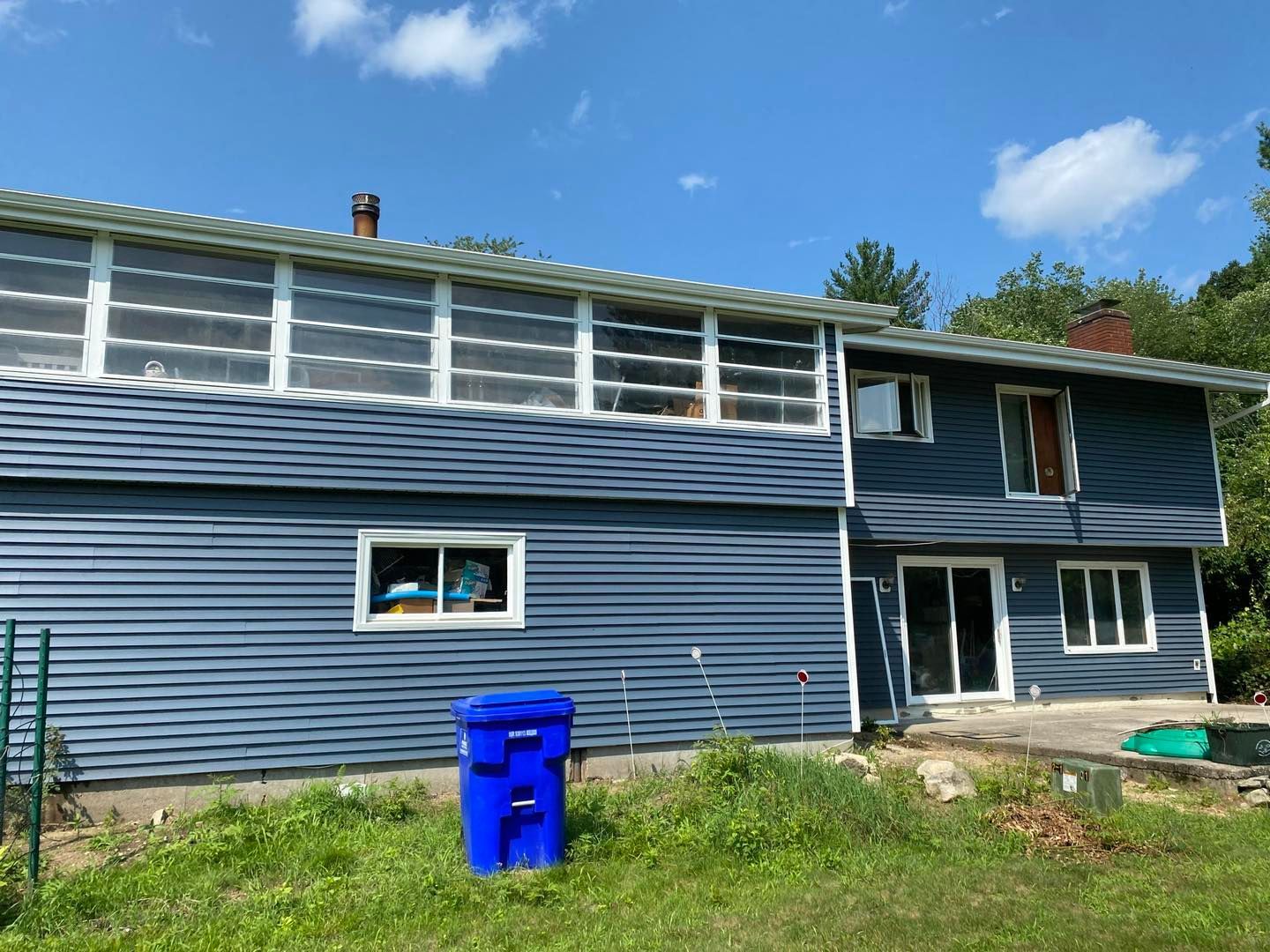 Blue-sided house with screen porch on top. A blue trash can sits in the front yard.