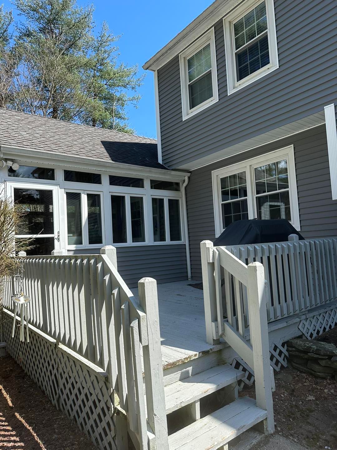 Wooden deck with steps leading to a gray house with white-framed windows and a sunroom.