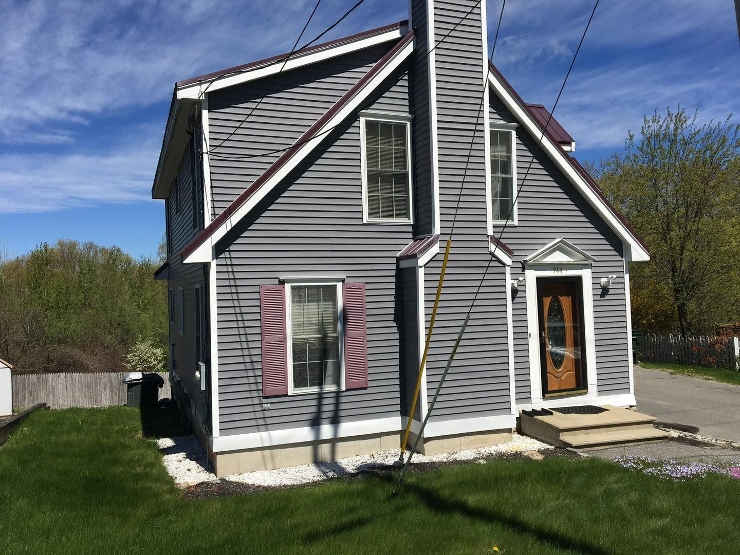 Gray house with purple trim and shutters, blue sky, and green grass.