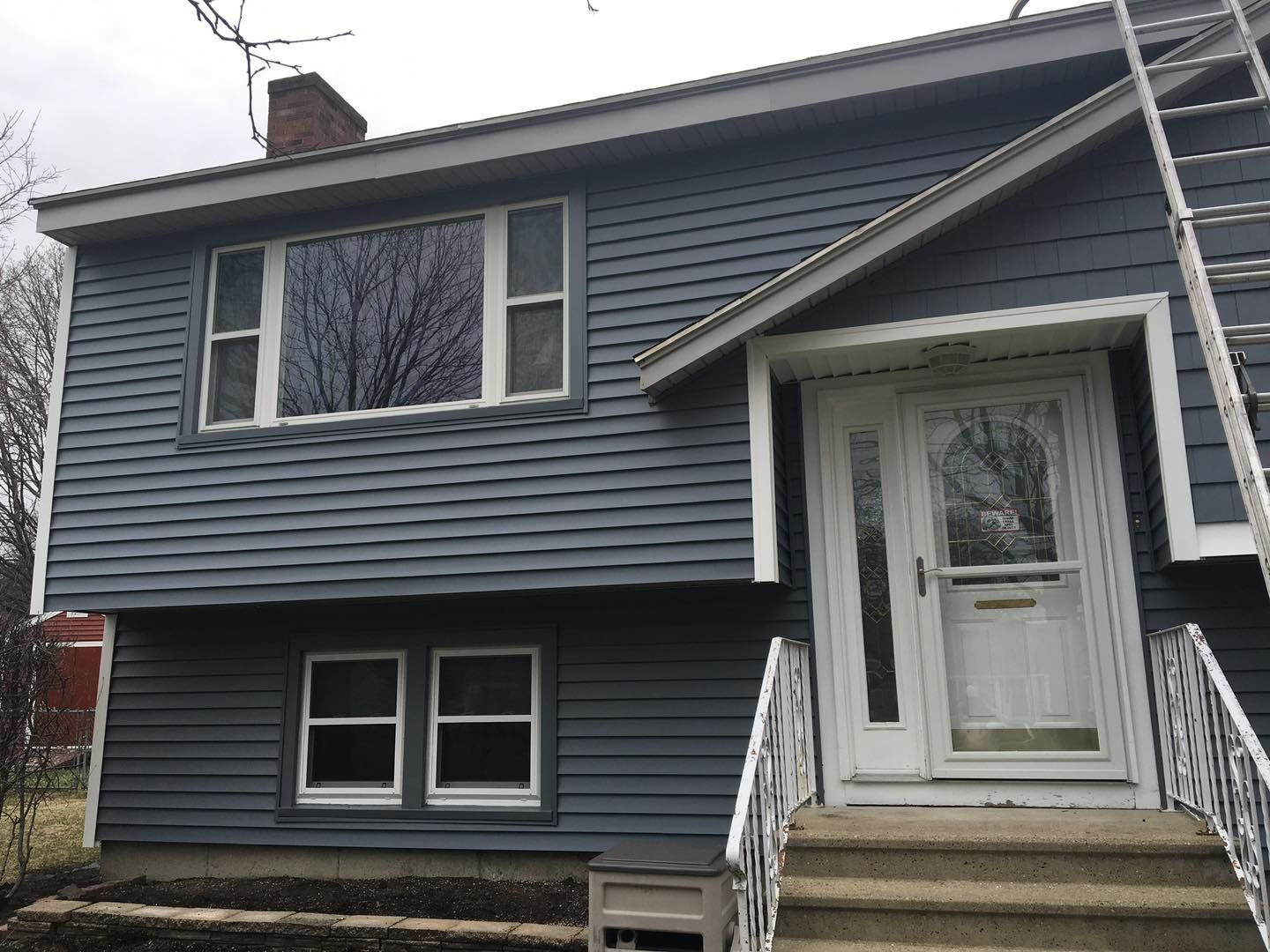 Blue-sided two-story house with white trim, windows, and door, stairs lead to the front entrance.