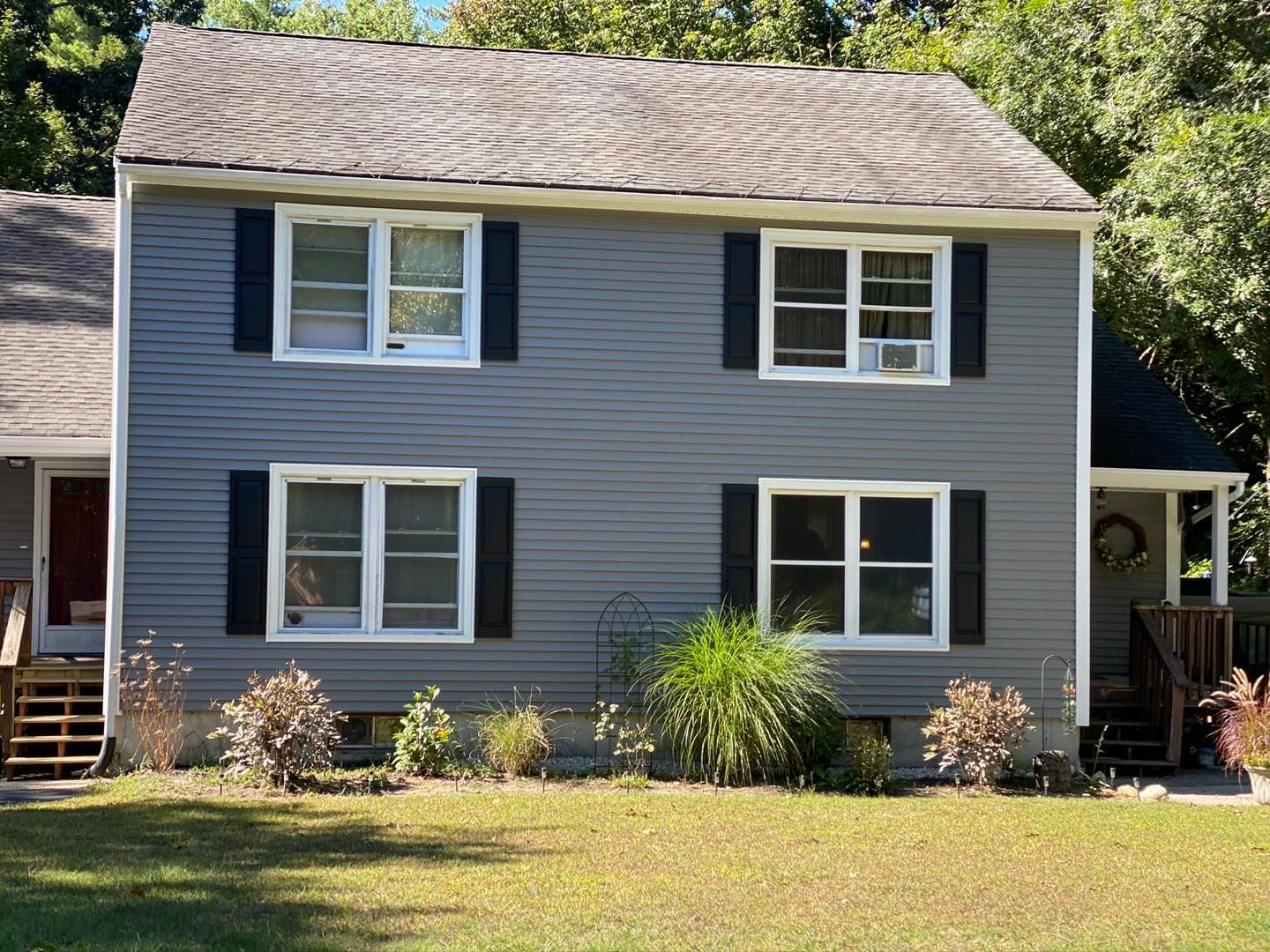 Gray two-story house with black shutters and white window frames. Green lawn and shrubbery in front.