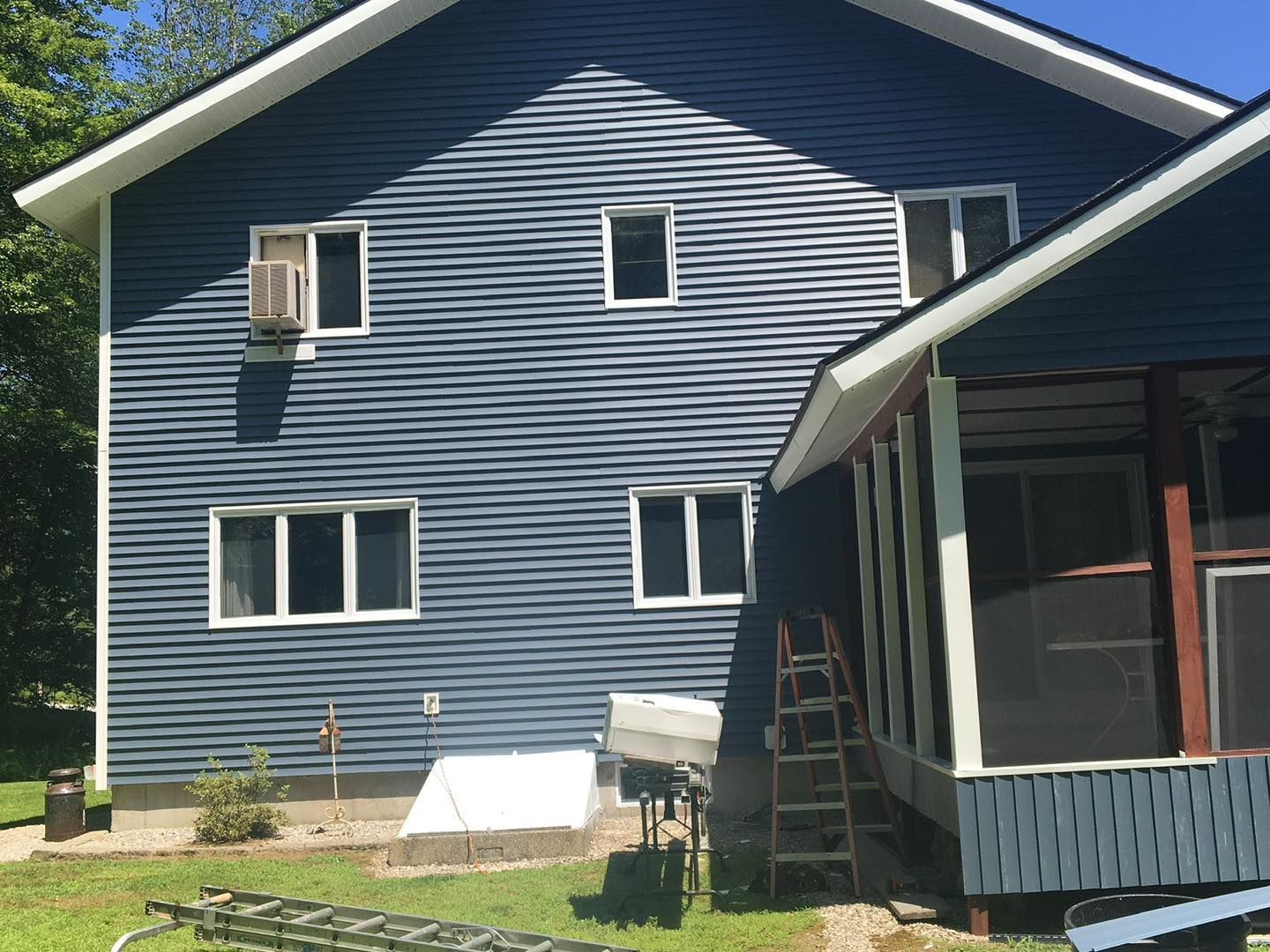 Blue-sided house with white-framed windows and a porch. A/C unit on the side, and a ladder.