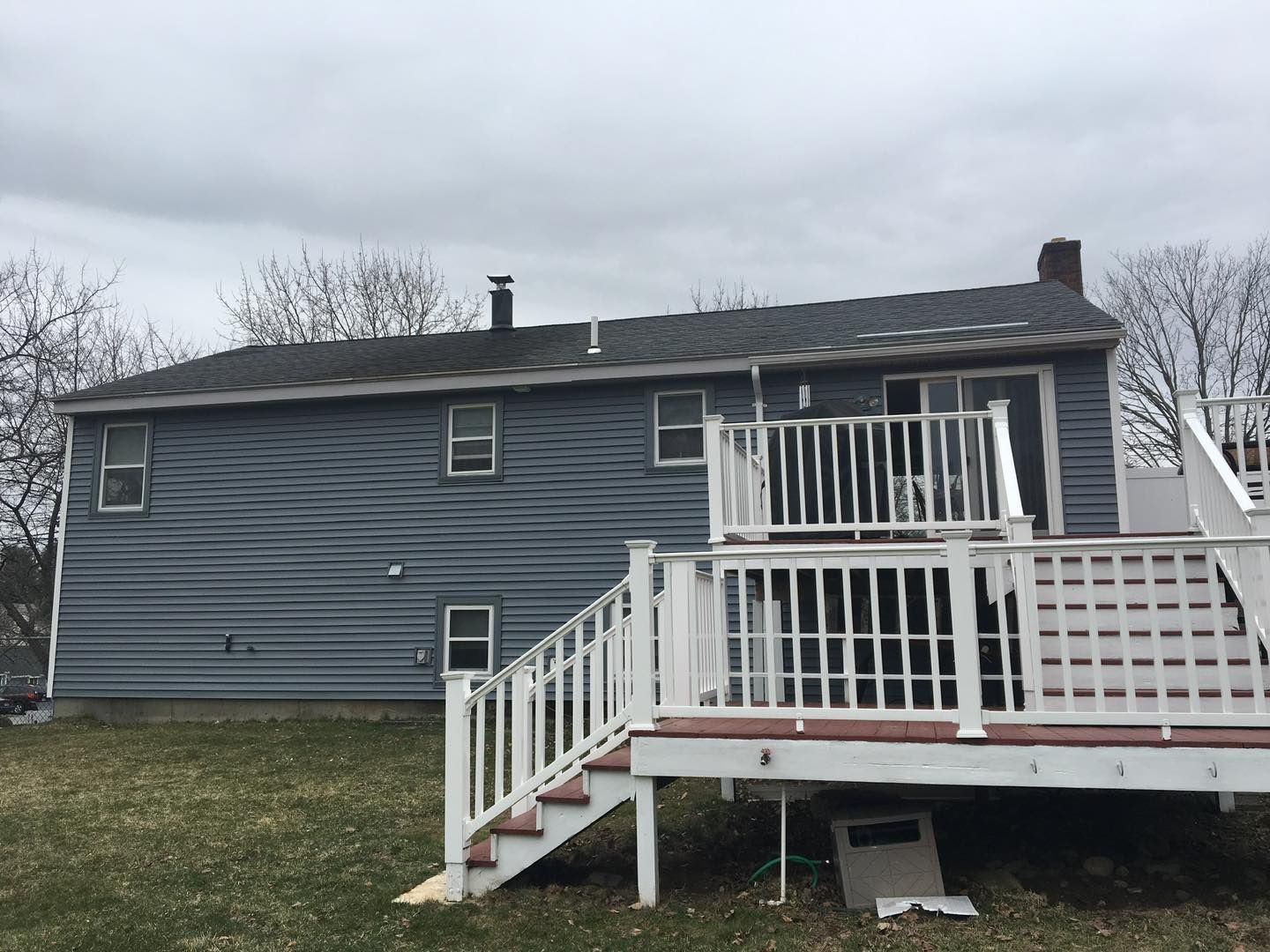 Back of a house with blue siding and a white deck, overcast sky.