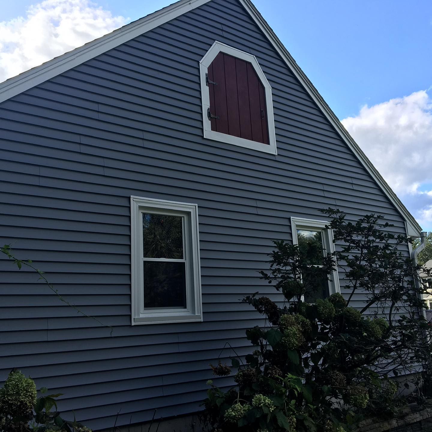 Gray house with red arched window, white trim, and two windows, against a blue sky.