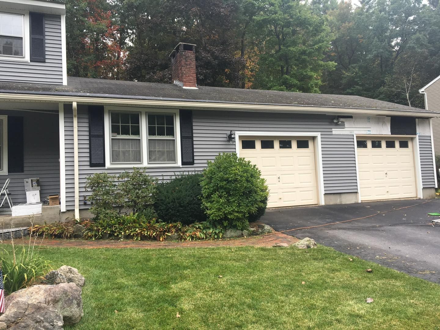 Gray house with two garage doors, a brick chimney, and a green lawn.