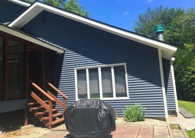Blue sided house with white trim, window, grill, and wooden stairs.