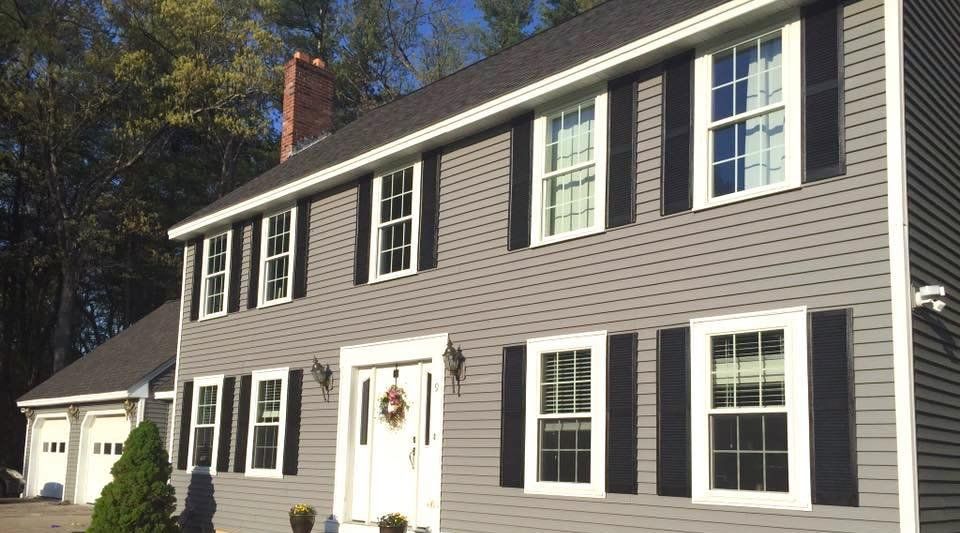 Gray house with black shutters, white door, and brick chimney.