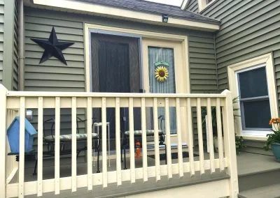 A porch with a cream-colored railing and light green siding. A black star, door, and window are visible.