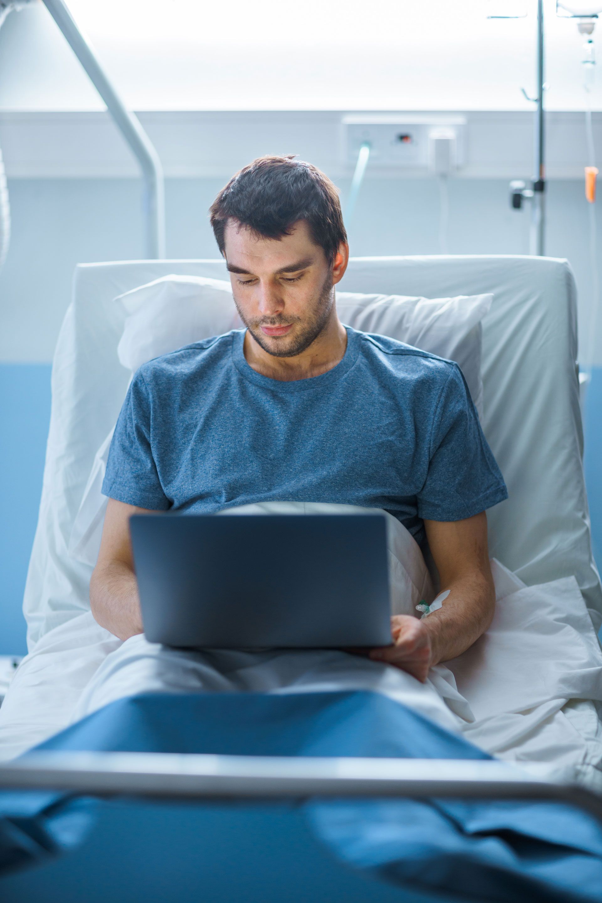 A man is laying in a hospital bed using a laptop computer.