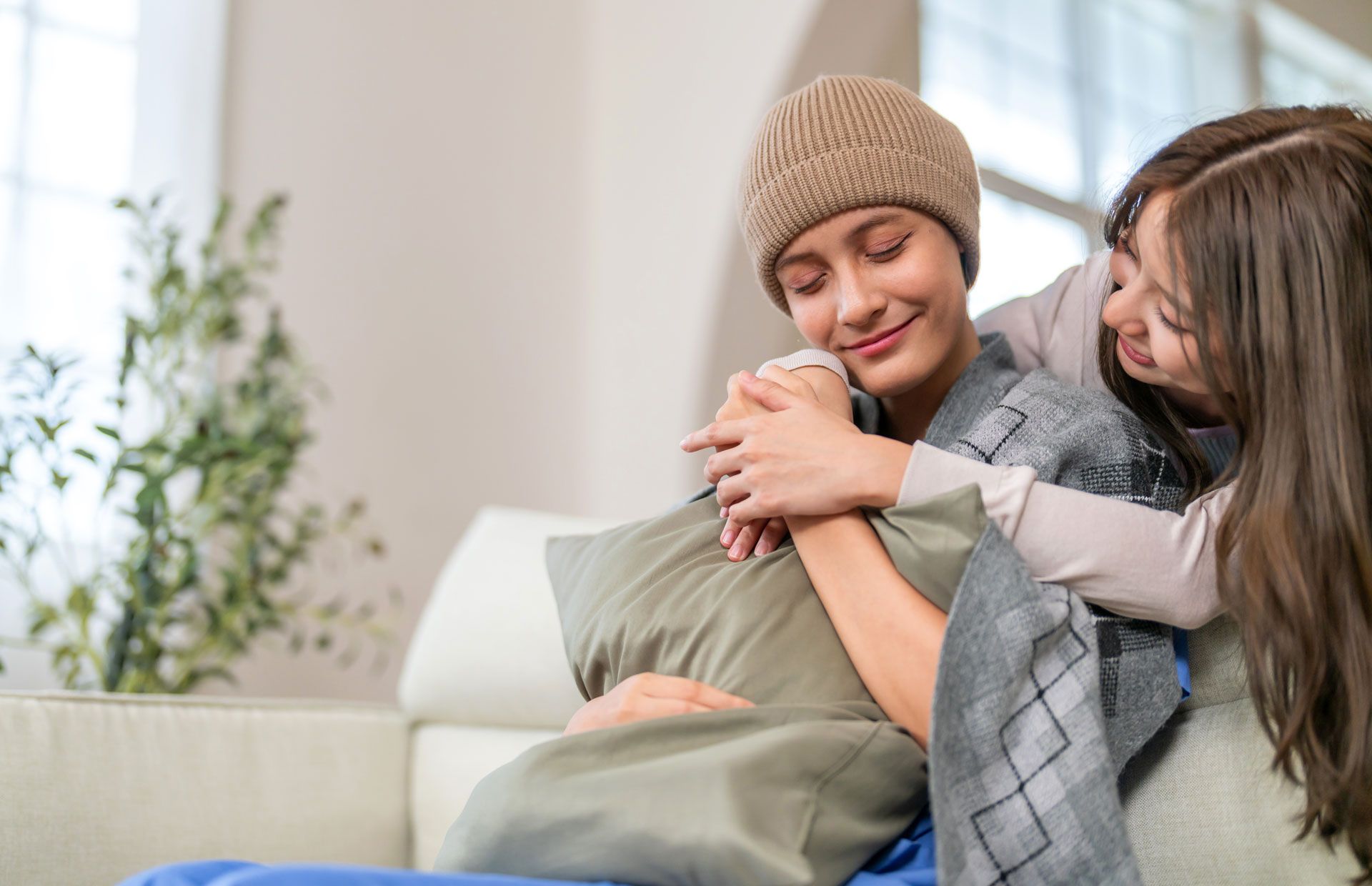 A woman with cancer is sitting on a couch with her daughter.