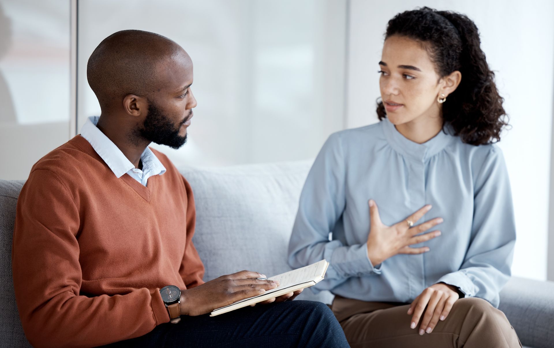 A man and a woman are sitting on a couch talking to each other.
