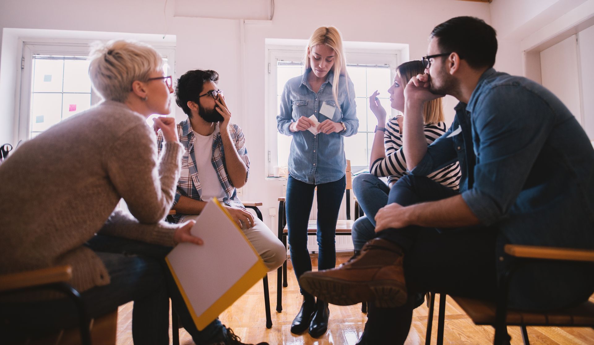 A group of people are sitting in a circle talking to each other in a room.
